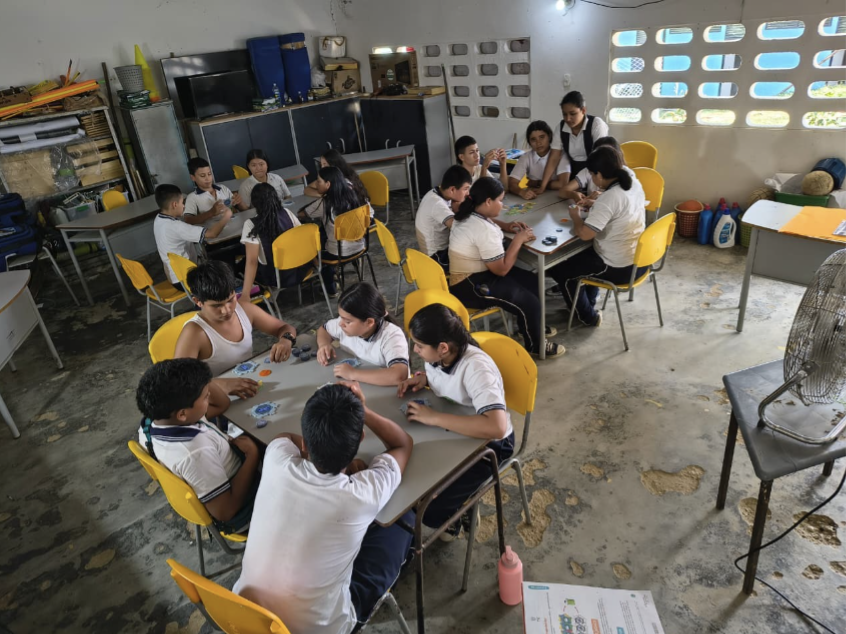 Estudiantes realizan una actividad grupal en mesas dentro de un salón de clases.