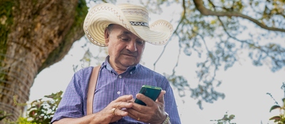 Foto de un campesino utilizando su celular bajo un árbol.