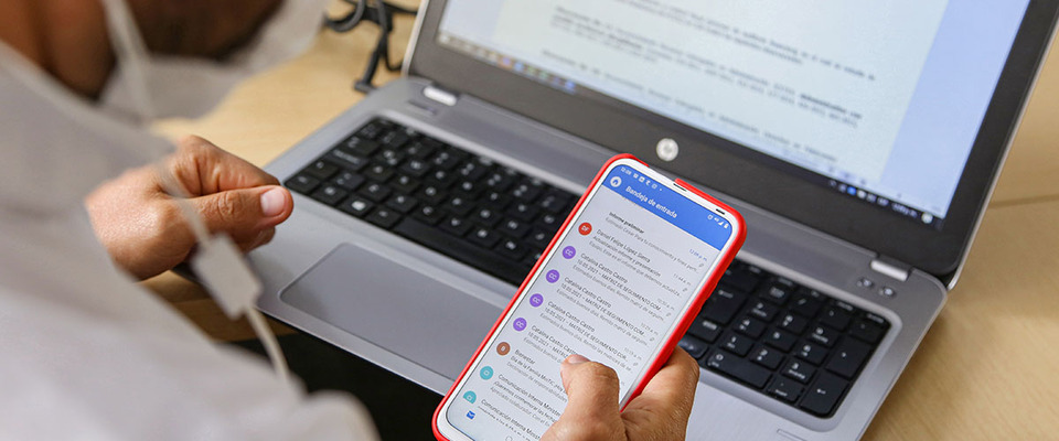 Foto de usuario usando un portatil y consultando su móvil