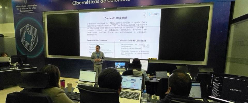 Experto expone sobre ciberseguridad ante un grupo de asistentes con portátiles, frente a una pantalla con información sobre contexto regional y protección digital