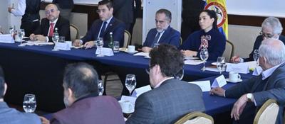 Funcionarios y técnicos se reúnen en mesa formal con bandera de Colombia, revisando documentos sobre auditoría del software electoral