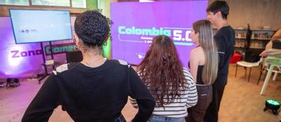 Jóvenes observan una pantalla en zona interactiva de Colombia 5.0, con luces de colores y ambiente tecnológico en Manizales