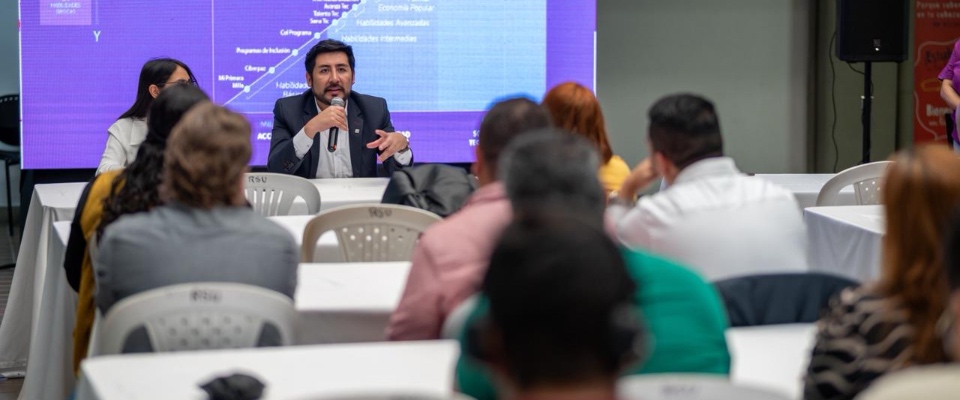 Hombre con micrófono expone ante público sentado; detrás, pantalla con gráficos sobre innovación y transformación digital en evento