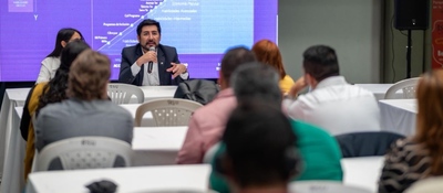 Hombre con micrófono expone ante público sentado; detrás, pantalla con gráficos sobre innovación y transformación digital en evento
