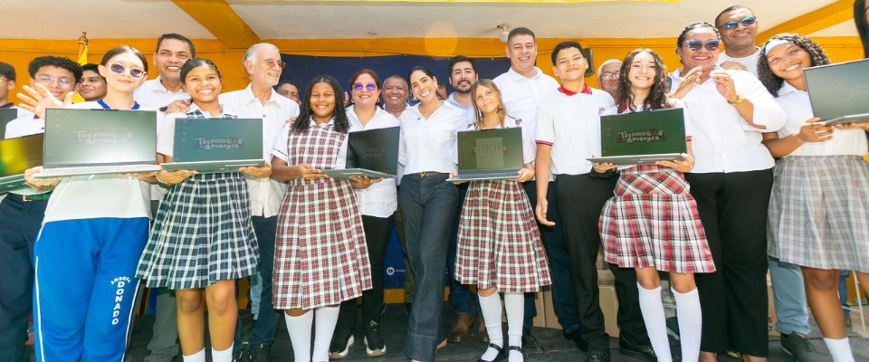 Grupo de estudiantes con uniformes escolares sostienen portátiles, acompañados de adultos, en un evento de entrega tecnológica en Atlántico