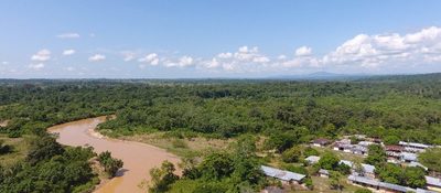 Vista aérea de un río marrón que serpentea entre selva densa; a un lado, un pequeño caserío rural rodeado de verde en el Magdalena Medio.