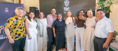 Grupo de nueve adultos posa sonriente frente a fondo con logo TIC; evento anuncia convocatorias audiovisuales Historias del Cambio.