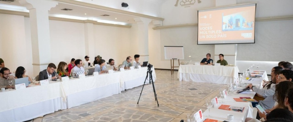 Participantes en mesas en U escuchan panel frente a pantalla sobre AMI; encuentro en Cartagena busca frenar desinformación y promover derechos.
