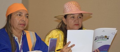 Dos mujeres, una con chaleco y otra con sombrero, revisan un documento en reunión sobre formación docente en inteligencia artificial.