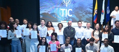 Grupo de jóvenes y adultos sostiene certificados en tarima; detrás, pantalla de MinTIC y banderas. Evento destaca liderazgo femenino.
