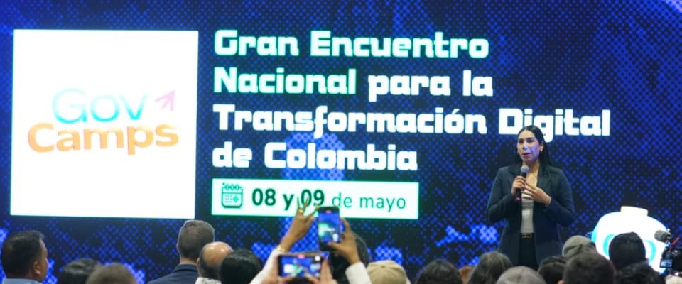 Auditorio lleno durante GovCamp 2026. En pantalla gigante anuncian encuentro nacional sobre transformación digital en Colombia.