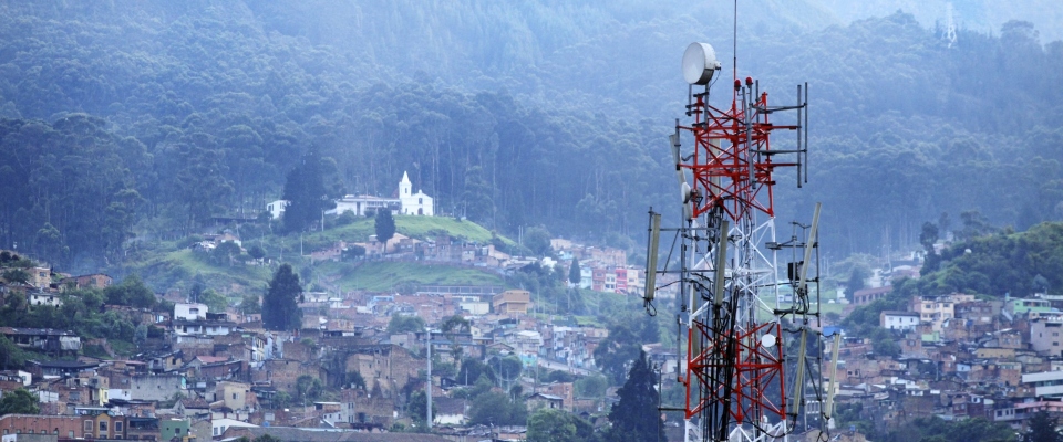 Antena de telecomunicaciones domina un barrio urbano rodeado de montañas y bosque, símbolo de conectividad y uso del espectro