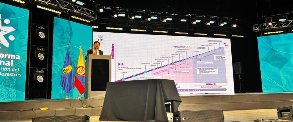 Funcionario presenta sistema digital de gestión del riesgo en escenario con pantallas y banderas institucionales