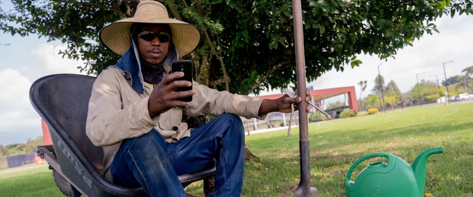 Trabajador rural usa celular mientras descansa en zona verde, reflejando expansión de conectividad en municipios del país
