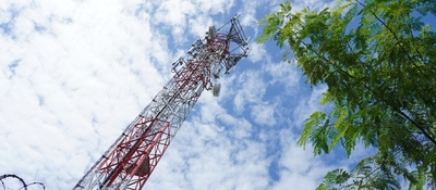 Antena de telecomunicaciones se eleva junto a árboles y cielo nublado, representando conectividad e infraestructura.
