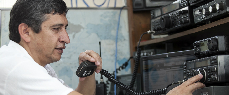 Hombre opera equipos de radio y sostiene un micrófono en estación de comunicaciones para radioaficionados