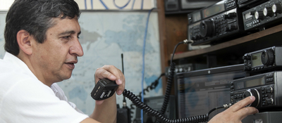 Hombre opera equipos de radio y sostiene un micrófono en estación de comunicaciones para radioaficionados