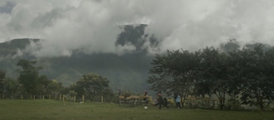 Paisaje rural con montañas cubiertas de niebla y personas en un campo, evocando la diversidad territorial del país