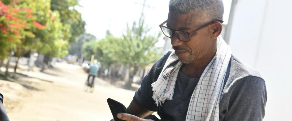 Hombre con gafas consulta su celular en una zona rural. La imagen representa acceso y conectividad para las comunidades