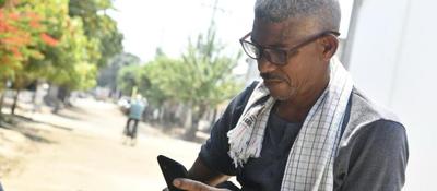 Hombre con gafas consulta su celular en una zona rural. La imagen representa acceso y conectividad para las comunidades