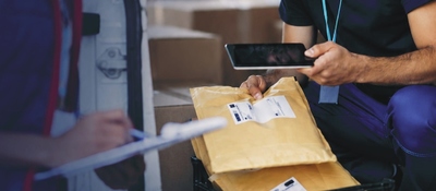 Operario registra paquetes con una tableta durante un proceso de entrega, reflejando la actividad del sector postal