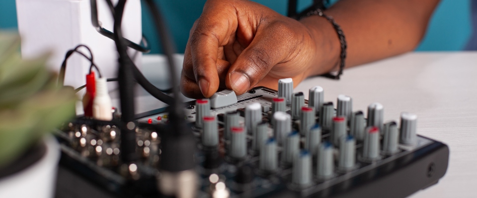 Una persona ajusta una consola de audio con varios controles, asociada a equipos de comunicación y radioafición