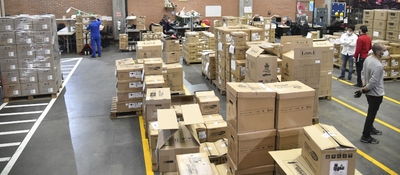 Bodega logística con decenas de cajas apiladas y trabajadores organizando envíos en amplios pasillos señalizados