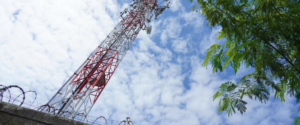 Torre de telecomunicaciones vista desde abajo, con antenas sobre estructura metálica y cielo parcialmente nublado.