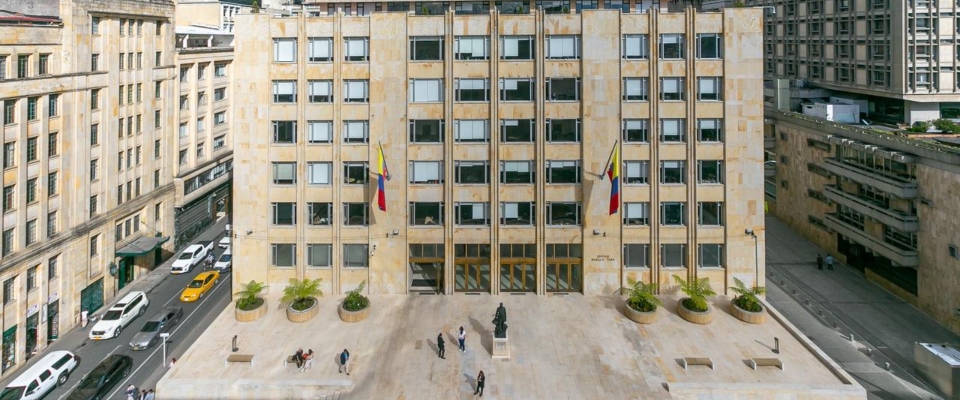 Fachada del edificio del Ministerio TIC en Bogotá, con banderas de Colombia y personas en la plaza frente al ingreso