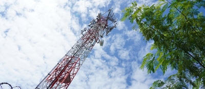 Torre de telecomunicaciones vista desde abajo entre árboles y cielo nublado. Ilustra el uso y gestión del espectro radioeléctrico.