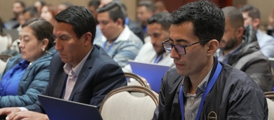 Personas sentadas con portátiles en una sala; al frente, un hombre con gafas mira su pantalla y otros observan sus equipos