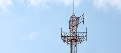 Parte superior de una torre metálica con antenas sobre cielo azul con nubes blancas dispersas.