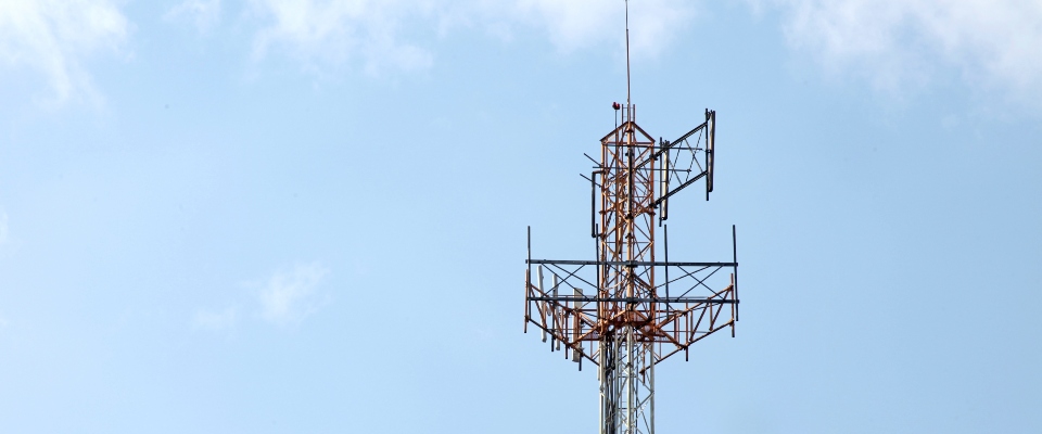 Antena de telecomunicaciones metálica con múltiples paneles y cables, sobre un cielo azul con nubes.