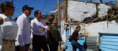 Cuatro personas observan una vivienda parcialmente derrumbada; otra mujer está sentada frente a la fachada dañada