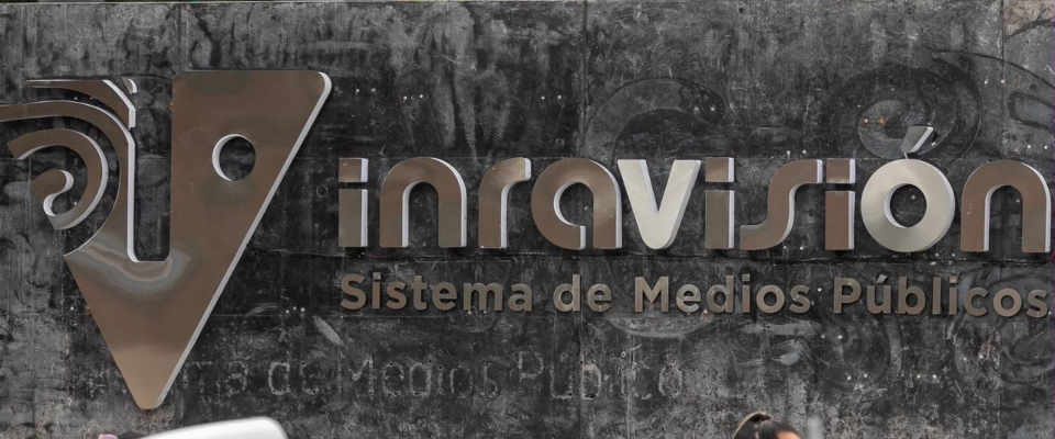 Cartel metálico sobre fondo gris oscuro, con un logotipo y el texto "Sistema de Medios Públicos" Cartel metálico sobre fondo gris oscuro, con un logotipo y el texto "Sistema de Medios Públicos"