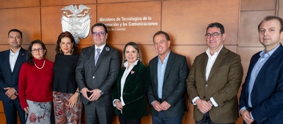 Ocho personas posan de pie ante una pared de madera con emblema y texto del Ministerio de Tecnologías de la Información y las Comunicaciones