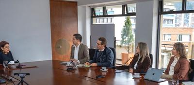 Cuatro personas sentadas alrededor de una mesa en una sala de reuniones; hay laptops, micrófonos y documentos