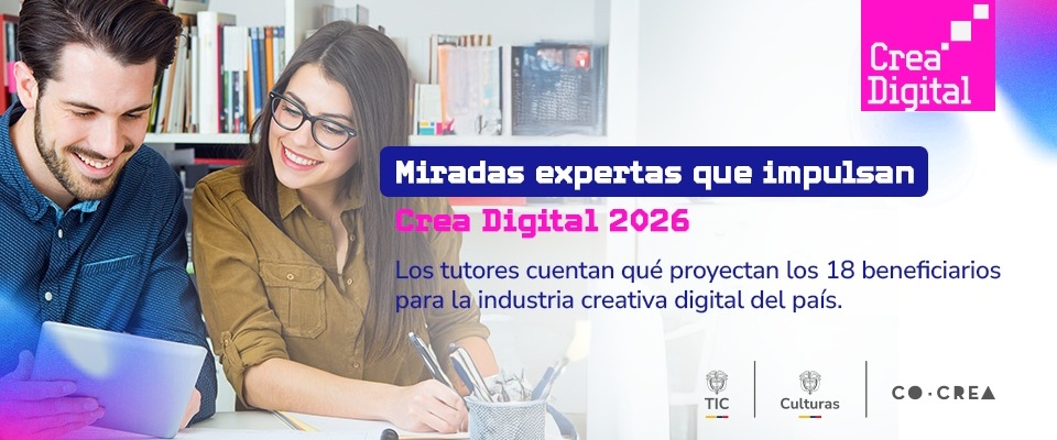 Dos personas sonríen mientras trabajan frente a una computadora y una tableta; detrás hay libros y materiales de escritorio.