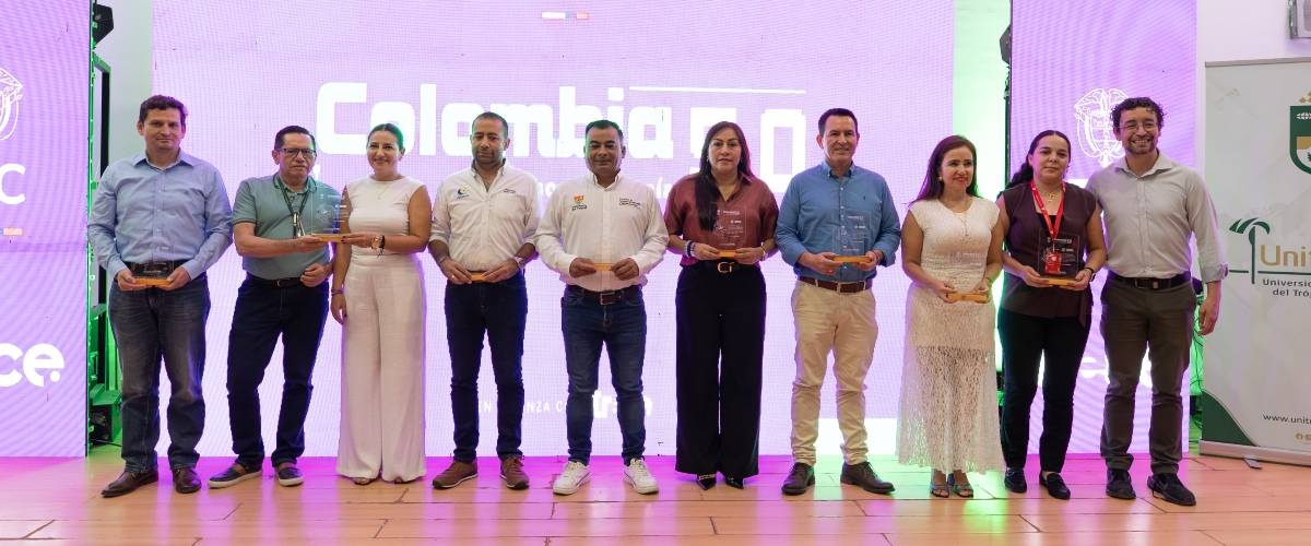 Diez personas posan en un escenario; sostienen reconocimientos frente a una pantalla iluminada con Colombia 5.0