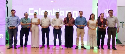 Diez personas posan en un escenario; sostienen reconocimientos frente a una pantalla iluminada con Colombia 5.0