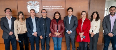 Nueve personas posan de pie frente al logo y nombre del Ministerio TIC; visten prendas en tonos oscuros, rojo, beige y gris