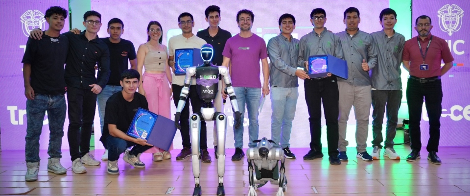 Grupo de personas posa junto a dos robots; algunos sostienen reconocimientos frente a una pantalla iluminada