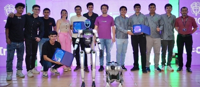 Grupo de personas posa junto a dos robots; algunos sostienen reconocimientos frente a una pantalla iluminada