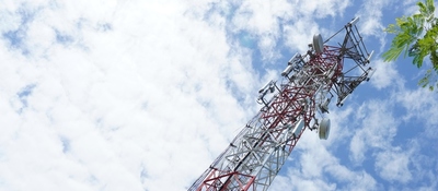 Torre metálica de telecomunicaciones inclinada hacia la esquina superior derecha, con antenas y cielo azul con nubes.