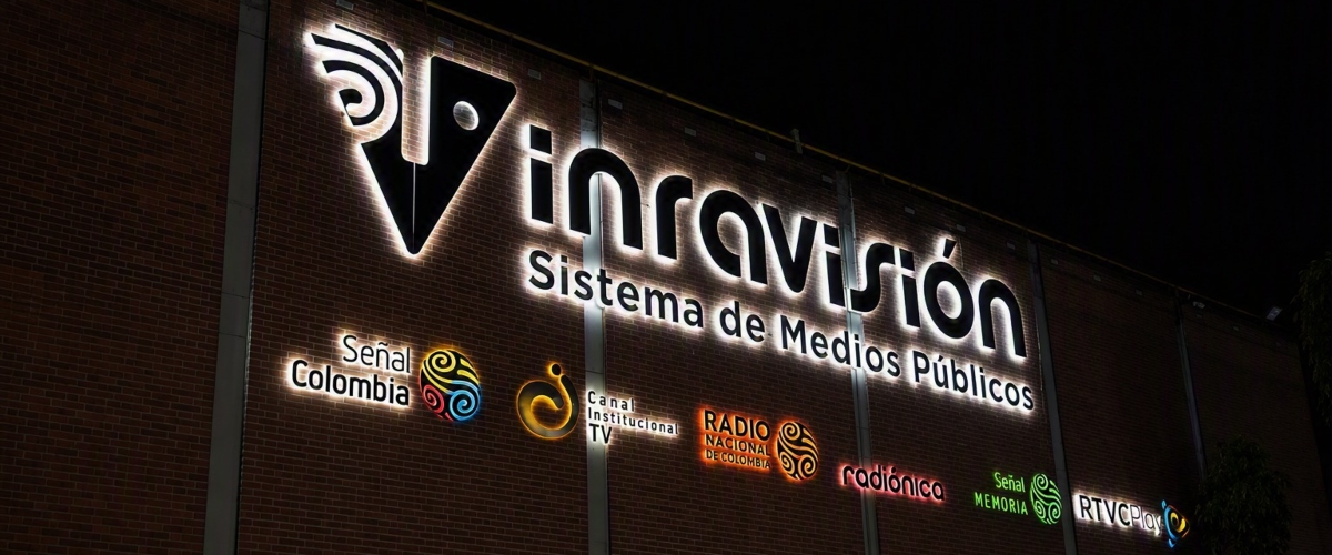 Fachada con letrero iluminado de RTVC Sistema de Medios Públicos y varios logotipos.
