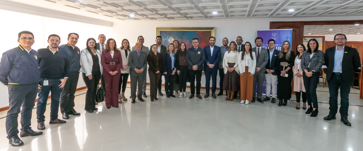 Grupo de personas posa de pie en un salón; al fondo hay un cuadro, una pancarta y mobiliario.