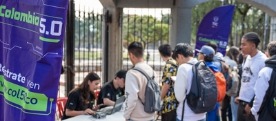 Personas hacen fila junto a una mesa con equipos tecnológicos. Un pendón de Colombia 5.0 aparece a la izquierda.
