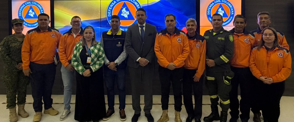 Once personas posan frente a pantallas con el emblema de la Defensa Civil; varias visten uniformes naranjas.