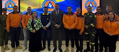 Once personas posan frente a pantallas con el emblema de la Defensa Civil; varias visten uniformes naranjas.