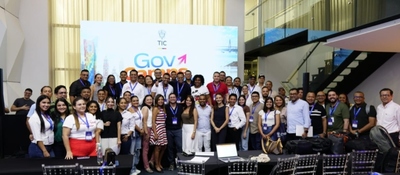 Fotografía grupal de participantes del evento GovCamp, realizado en un espacio institucional del sector TIC. Cerca de 50 personas posan frente a un pendón con la imagen de GovCamp.